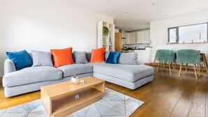 Un salon moderne avec un canapé d’angle gris, une table basse en bois et un coin repas comprenant deux chaises.