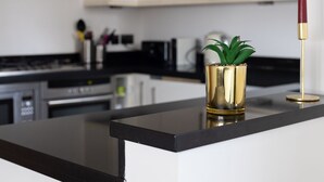 Une cuisine moderne avec un plan de travail noir, un vase doré contenant une plante verte et une lampe rouge.