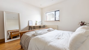 Une chambre à coucher comprenant un lit, un bureau, une chaise, un miroir et une fenêtre donnant sur la ville.