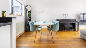 Une cuisine moderne avec un coin repas, comprenant une table ronde entourée de chaises turquoise, un piano noir et une grande horloge murale.