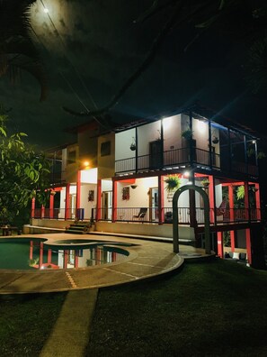 Un edificio de dos plantas con piscina, mobiliario exterior y un balcón.