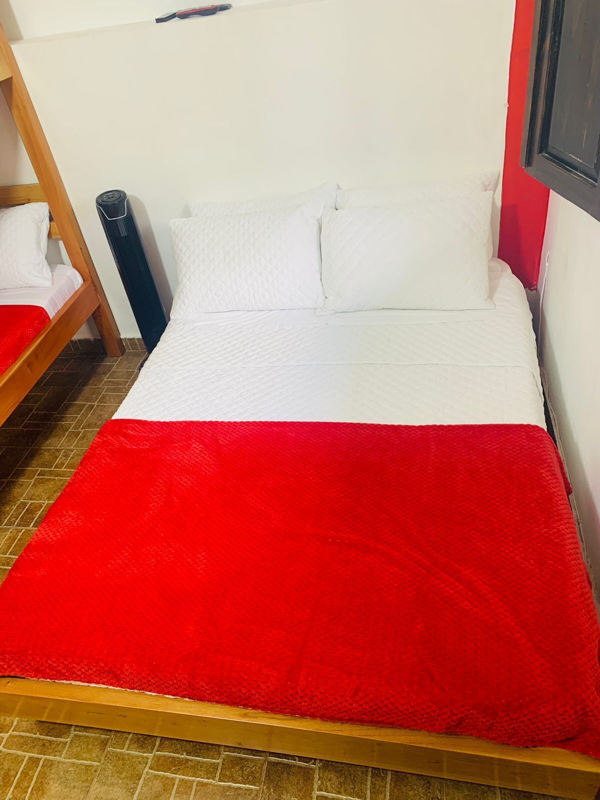 Uma cama de solteiro com cobertor vermelho, almofadas brancas e cabeceira de madeira.