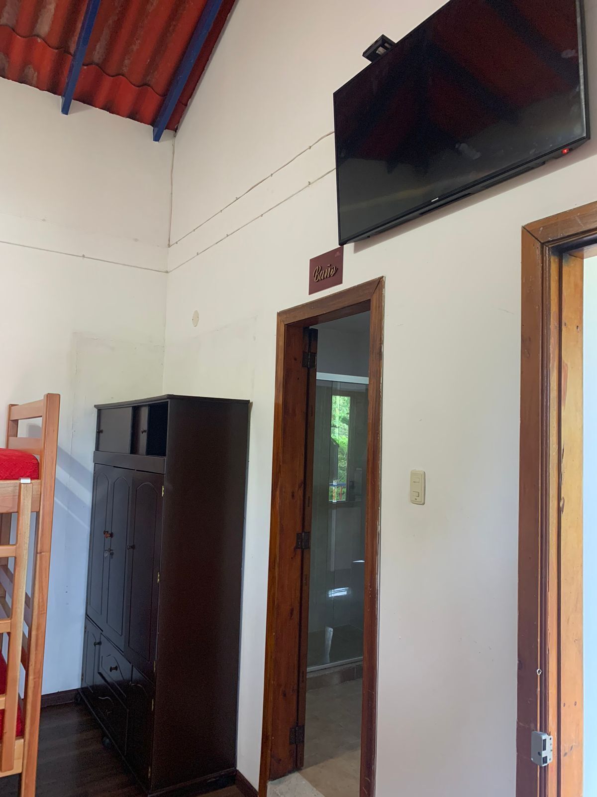 A room with a television mounted on the wall, a wooden door, and a wardrobe.