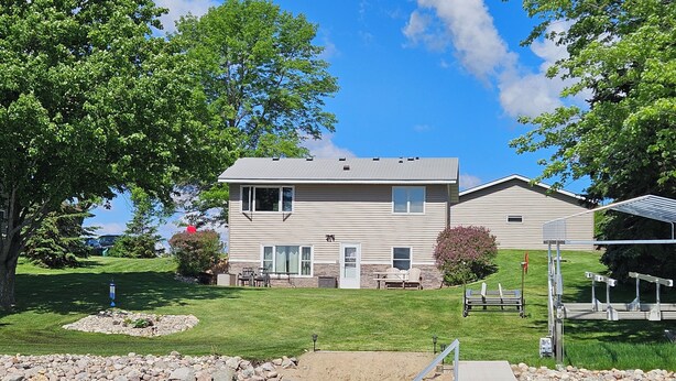 A two-story house with a dock extending into a lake, surrounded by a well-maintained lawn and trees.