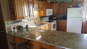 A kitchen with wooden cabinets, a granite countertop, a microwave, a refrigerator, and a sink.