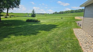 A well-maintained lawn with a small flower bed, a tree, and a gravel path leading to a house.