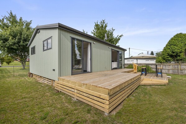 Un bâtiment d’un seul étage, de couleur vert clair, doté d’une terrasse en bois et de grandes portes-fenêtres coulissantes.