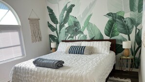 A bedroom with a bed, a window, a wall mural, a bedside lamp, and a rug. - Sun Kiss Villas - Beachside Duplex, Private Pool and Steps to Beach (Fort Myers Beach)
