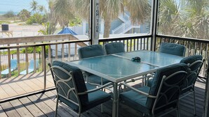 A covered outdoor area with a glass table and chairs, overlooking a pool and palm trees. - Sun Kiss Villas - Beachside Duplex, Private Pool and Steps to Beach (Fort Myers Beach)