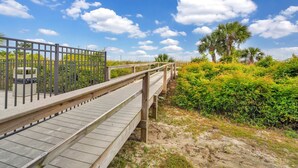 A wooden boardwalk leading to a beach with a fence and trash bin on the left. - Sun, Sand, Serenity -Savannah/Tybee (Tybee Island)