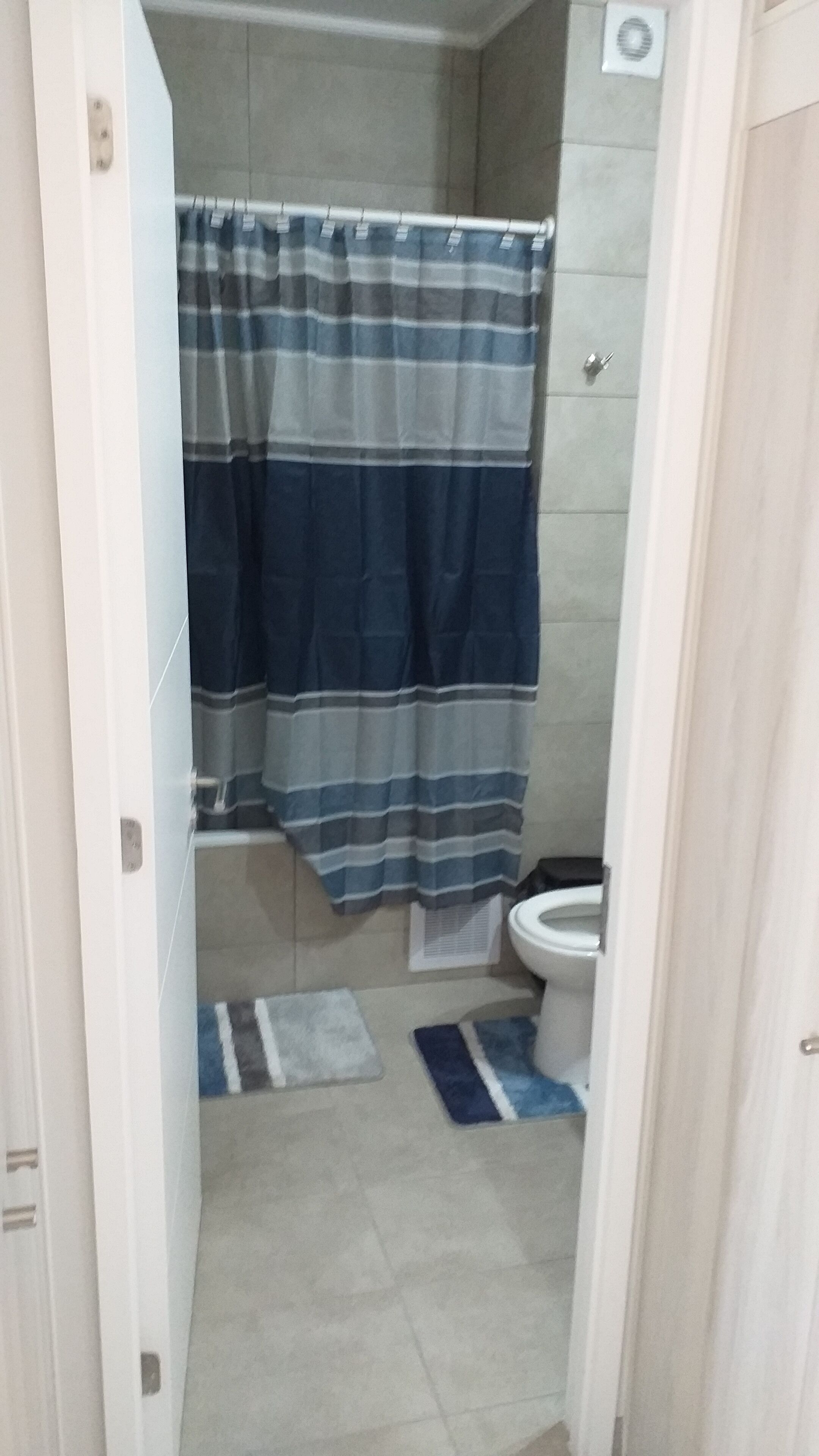 Et badeværelse med en stribet bruseforhæng, toilet og en lille måtte på gulvet.
