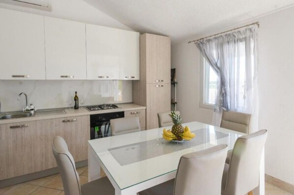 A modern kitchen with white cabinets, a dining table with chairs, and a window with sheer curtains. - Seclude charmy house with pool 200m from sea (Duboka)