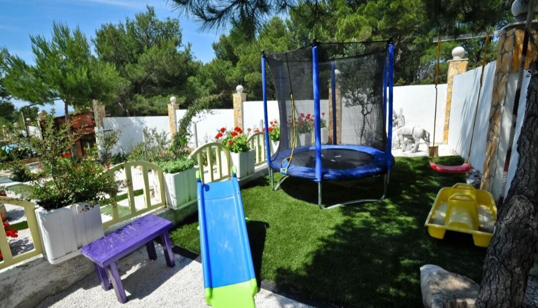 A backyard with a trampoline, a slide, a bench, and a tree.