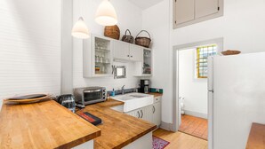 A compact kitchen with white cabinets, a wooden countertop, a toaster, a kettle, and hanging baskets.