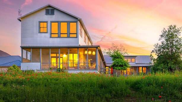 A two-story house with a porch and large windows, surrounded by a field of red flowers.