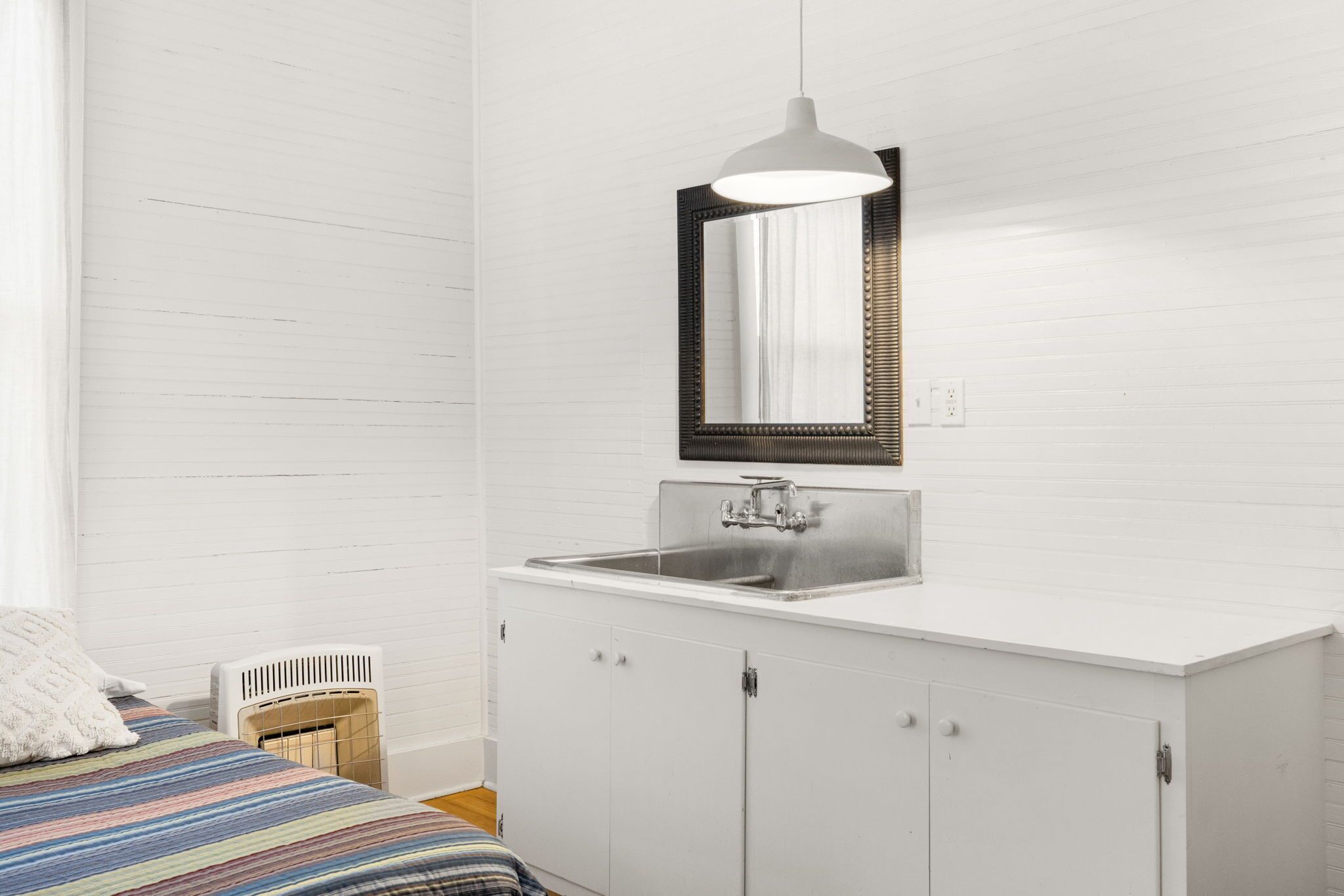 A small, clean room with a bed, a white radiator, a sink, and a mirror.