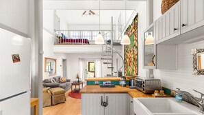 A modern kitchen with a central island, a dining area with a sofa, and a staircase leading to an upper level.