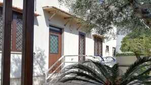 A building with a white exterior, wooden doors, and a staircase leading to a balcony. - Seaside B&B - Bright and breezy apartment with large garden 100 m from the sea. (Anzio)