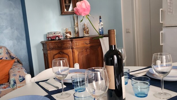 A dining table set with plates, glasses, a bottle of wine, and a decorative rose. - Seaside B&B - Bright and breezy apartment with large garden 100 m from the sea. (Anzio)