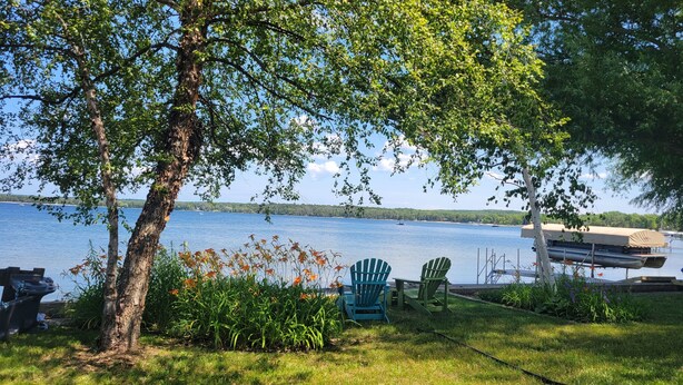 Vista al lago con un muelle, un bote cubierto y un área verde con sillas Adirondack.