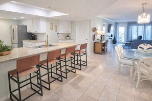 A modern kitchen with a central island, bar stools, and a dining area with white chairs.