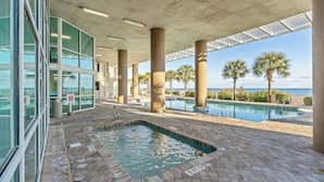 Zona de piscina interior con vistas al océano, pilares grandes y acceso mediante un edificio de vidrio.