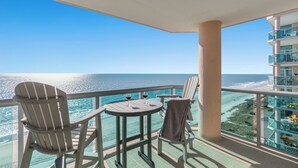 A balcony with two chairs, a small table, and two glasses of red wine.