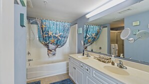 A bathroom with a bathtub, a double sink, and a shower curtain with a starfish design.