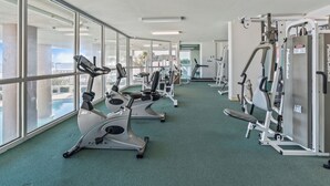 Un gimnasio con máquinas de cardio, equipo de entrenamiento con pesas y amplias ventanas con vistas al exterior.
