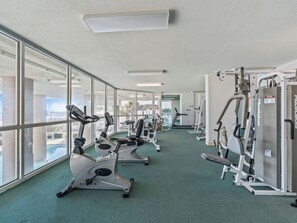 Un gimnasio con máquinas de cardio, equipo de entrenamiento con pesas y amplias ventanas con vistas al exterior.
