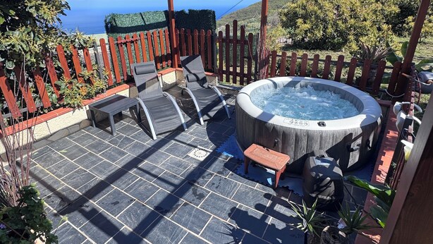 En täckt uteplats med ett bubbelbad, en sittgrupp och utsikt över havet.