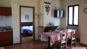Uma cozinha com uma mesa de jantar, uma cama, um cabideiro e uma janela com um relógio.
