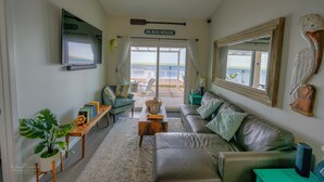 A living room with a leather sofa, a coffee table, and a TV mounted on the wall. There is a sign above the door that reads "BEACH HOUSE". - Bungalow on South Padre Bay (Port Isabel)