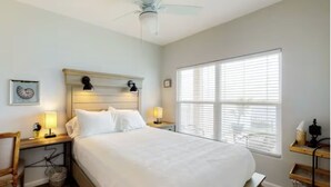 A neatly arranged bedroom with a large bed, two bedside lamps, a ceiling fan, and a window with blinds. - Bungalow on South Padre Bay (Port Isabel)