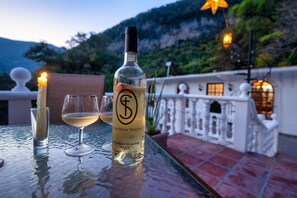 Pullo San Miguel de Allenden viiniä, lasi valkoviiniä ja sytytetty kynttilä pöydällä, jolta avautuu näkymä vuoristomaisemaan.
