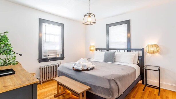 Ein modernes Schlafzimmer mit Bett, Nachttisch, Bank und einer Topfpflanze.