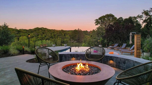 A fire pit surrounded by chairs, a pool, and lounge chairs in a landscaped outdoor area.