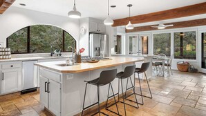 A modern kitchen with a large island, bar stools, and a dining area with a view of the outdoors.