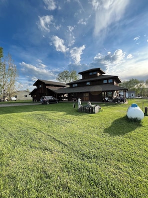 A large, multi-story wooden building with a spacious lawn in front. - Ski, Hike, bike, fish, hunt & Yellowstone. 4 bed, 3 bath with hot tub! Sleeps 8 (Clyde Park)