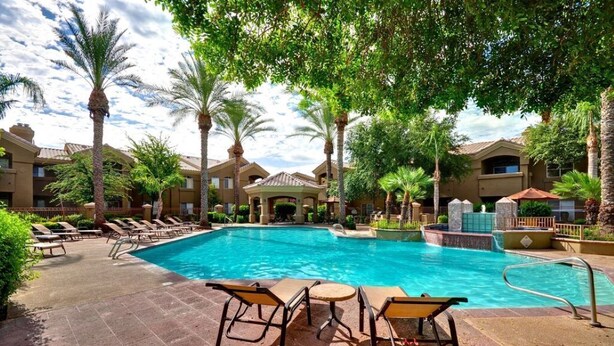 A swimming pool with lounge chairs and a gazebo, surrounded by palm trees and a building with a tiled roof. - Amazing Casita with Upgrades Galore! (Scottsdale)