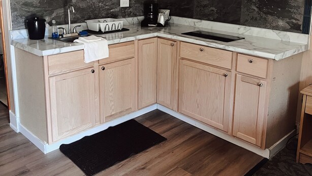 A modern kitchen with wooden cabinets, a white microwave, and a granite countertop. - Hampton Motel (Hampton)