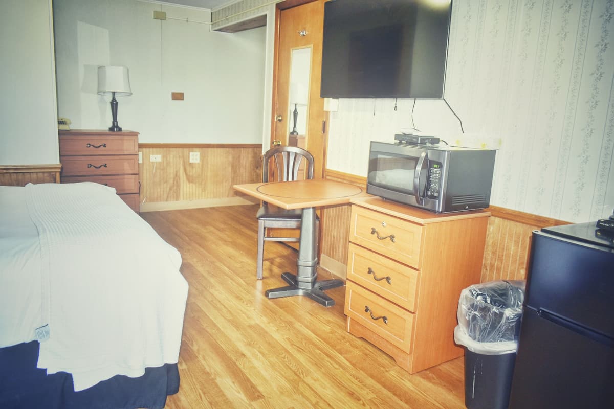 A hotel room with a bed, a desk with a microwave, a chair, a dresser, and a TV mounted on the wall.