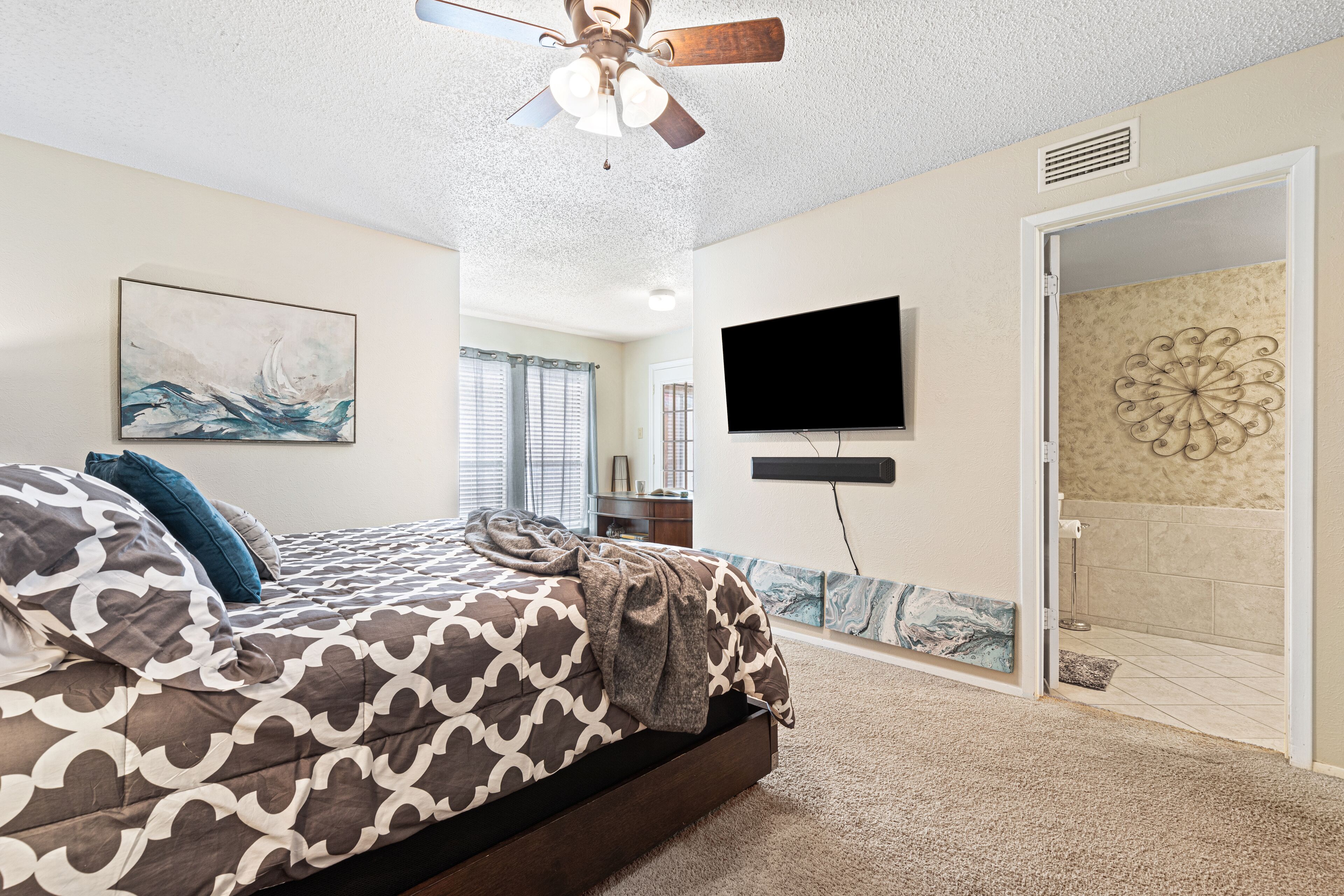 Ein Schlafzimmer mit Bett, Deckenventilator, Fernseher und Duschbereich.