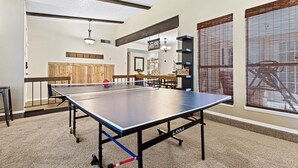 Et ping pong-bord i et rum med højt til loftet, træbjælker og udsigt gennem store vinduer med persienner.