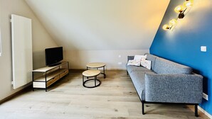 Moderni olohuone, jossa on televisio, sohva, sohvapöytä ja pieni sivupöytä.