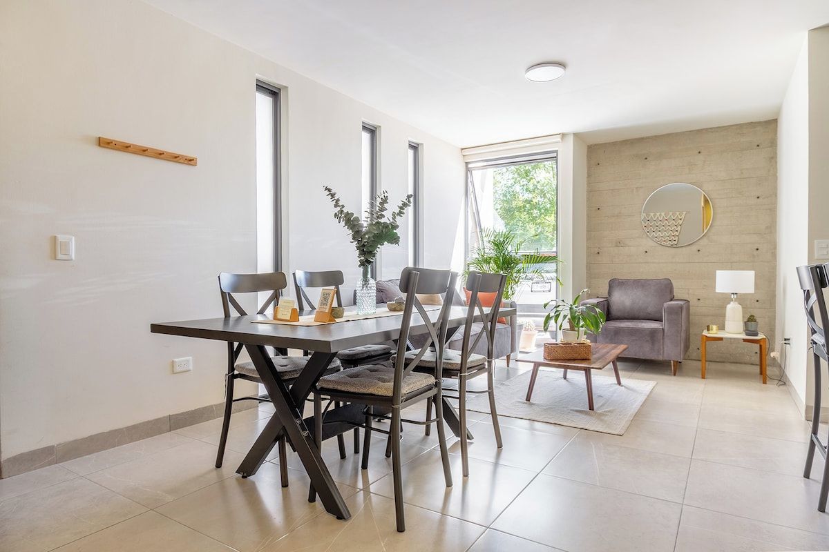 A modern living room with a dining area, large windows, and a grey sofa.