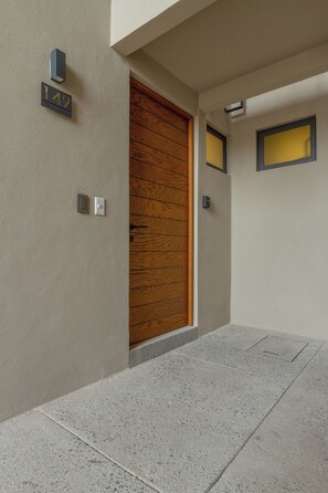 A building entrance with a wooden door, a number plaque, and a light switch.