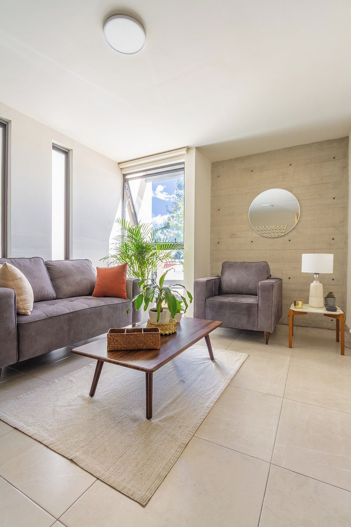 Un salon moderne avec deux canapés, une table basse, une table d’appoint avec une lampe et un grand miroir au mur.