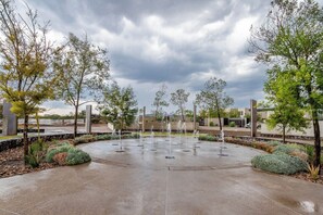Ein kreisförmiges Wasserspiel mit mehreren Brunnen, umgeben von Grünflächen und Bäumen.