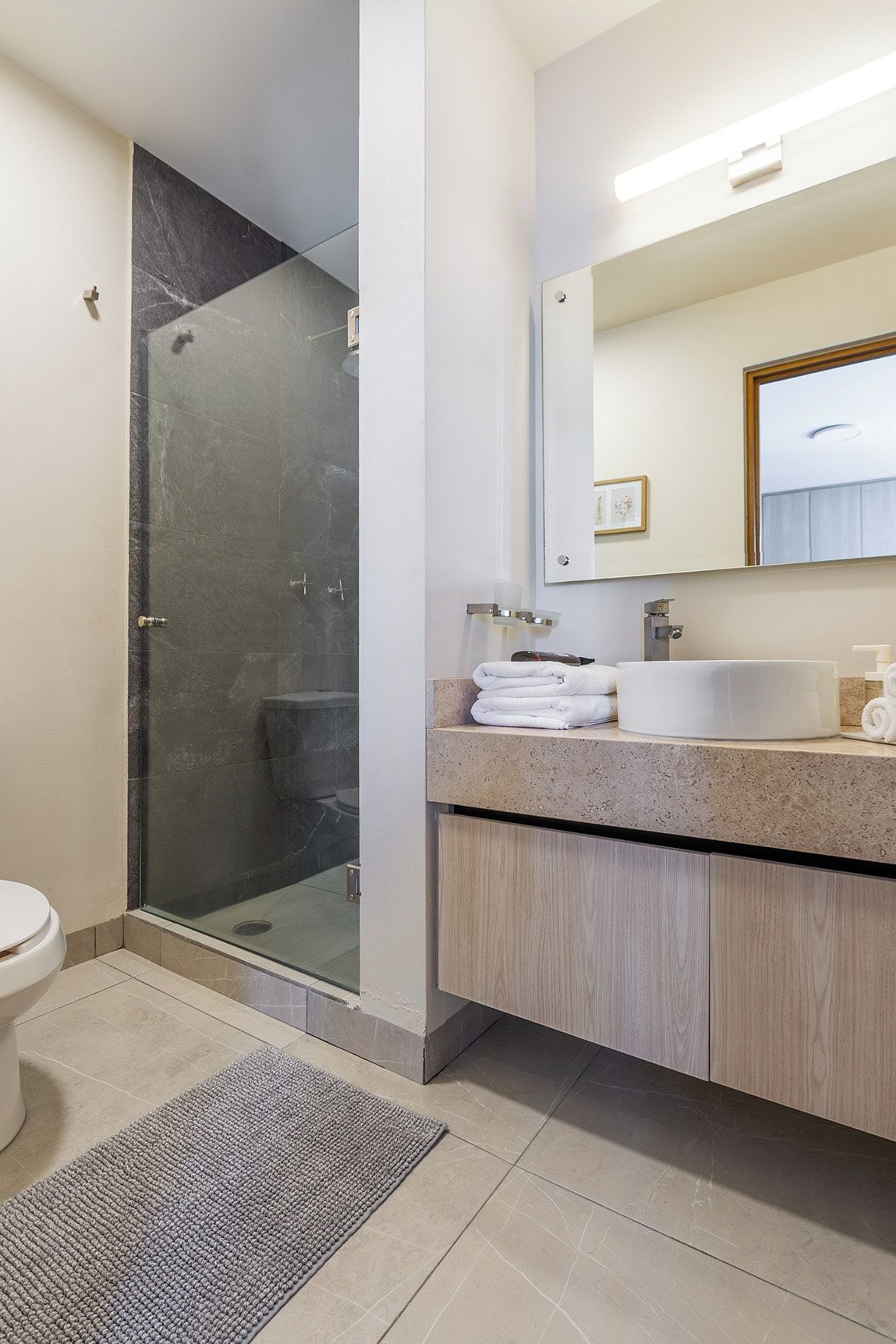A modern bathroom with a glass-enclosed shower, a white sink, and a wooden vanity.
